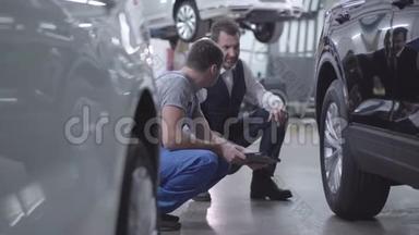 两个白种人成年男子坐在车旁边的舱里聊天。 专业维修人员，蓝袍咨询